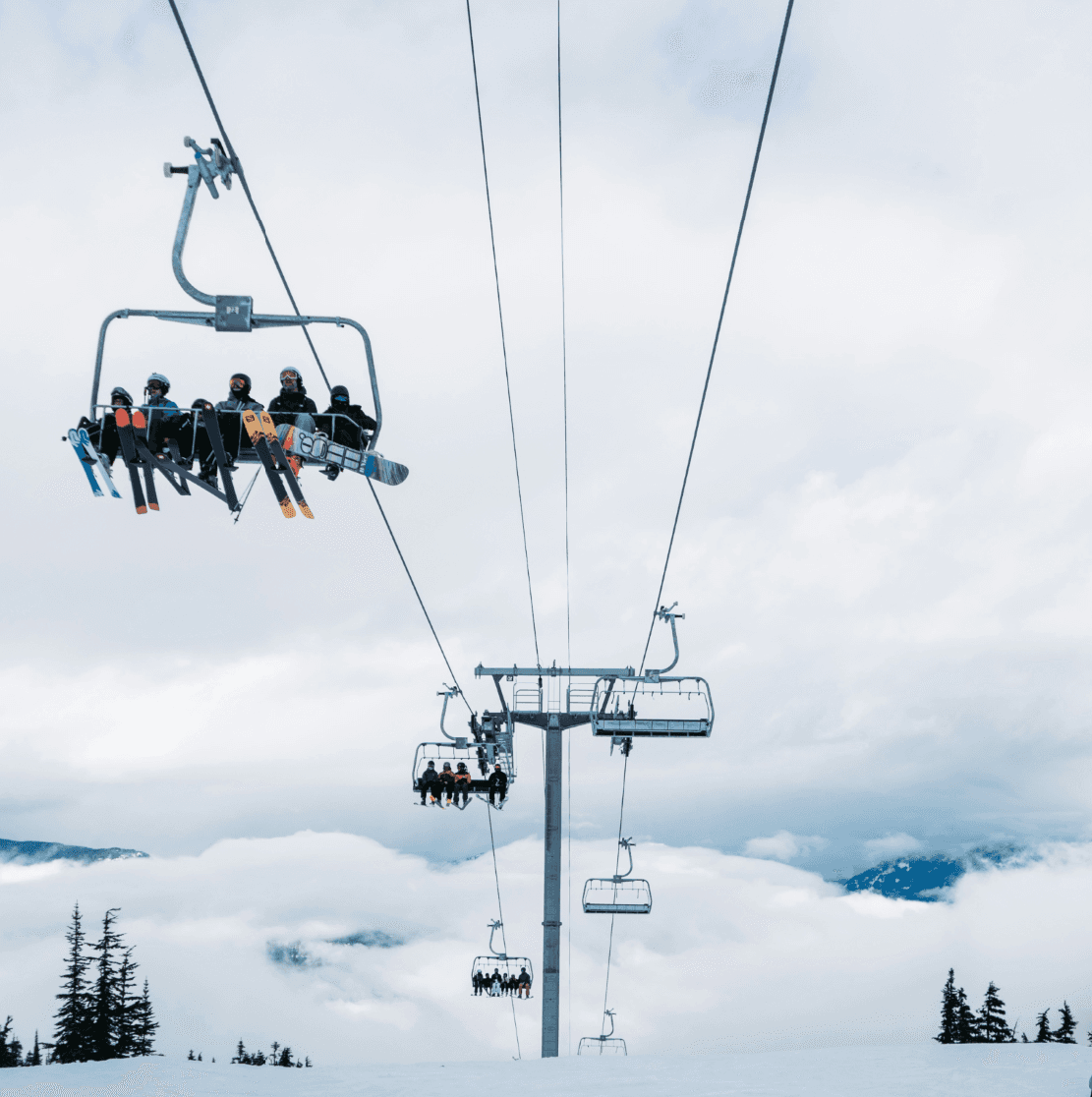 6 person chairlift coming over the hill at Whistler Blackcomb with skiers and snowboarders on it and mountains in the background