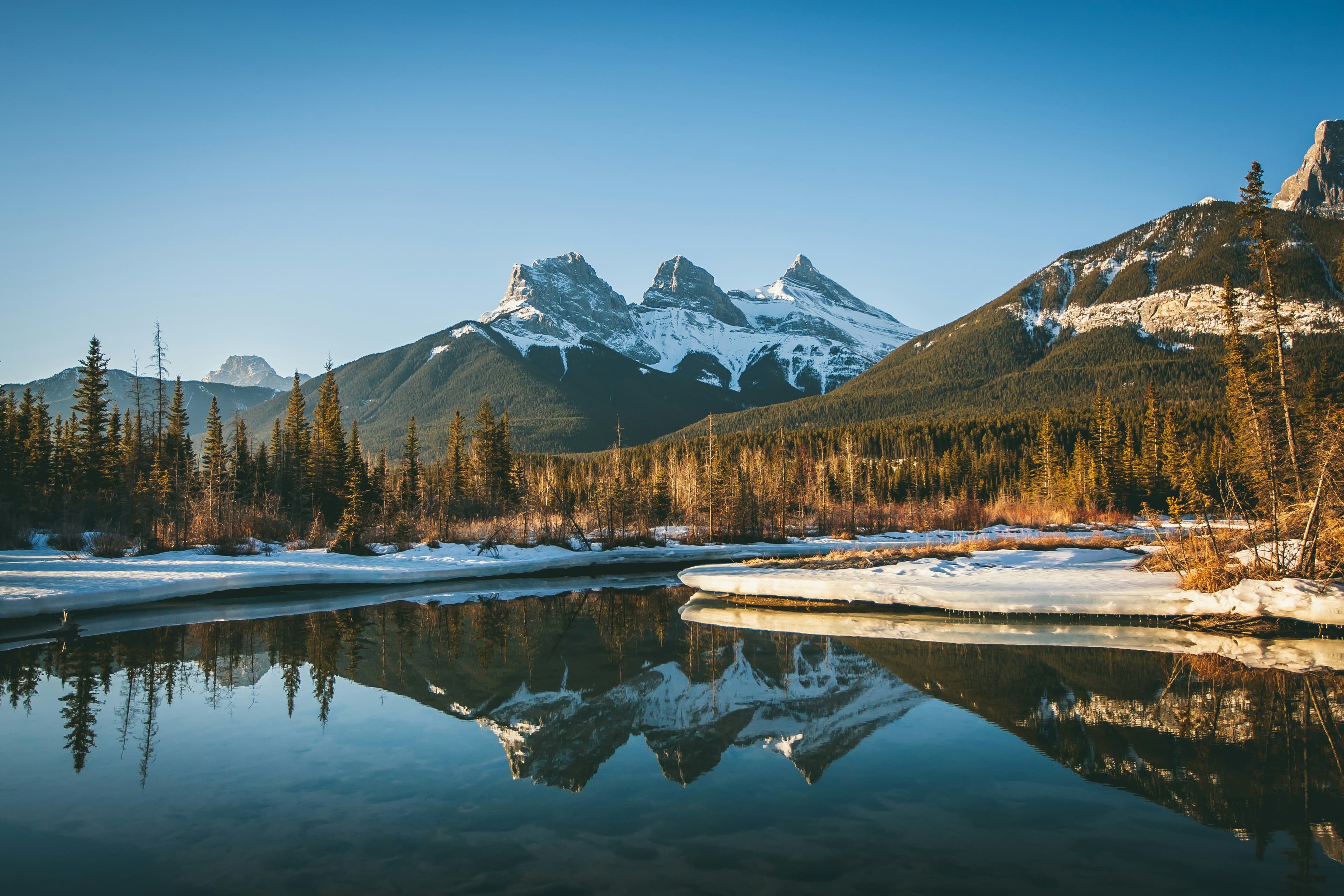 The three sisters mountain with forested hills and a snowy river in front